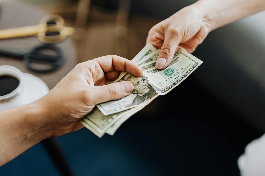 pexels photo 4968384 4968384 A close-up image of hands exchanging US dollar bills, symbolizing financial transaction or payment.