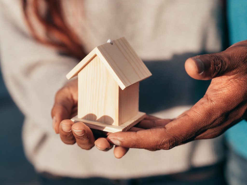 pexels photo 7579137 7579137 Close-up of hands holding a small wooden house, symbolizing real estate or home ownership.